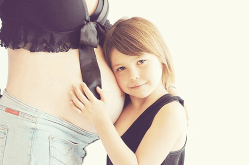 A young girl hugging her mothers pregnant stomach.